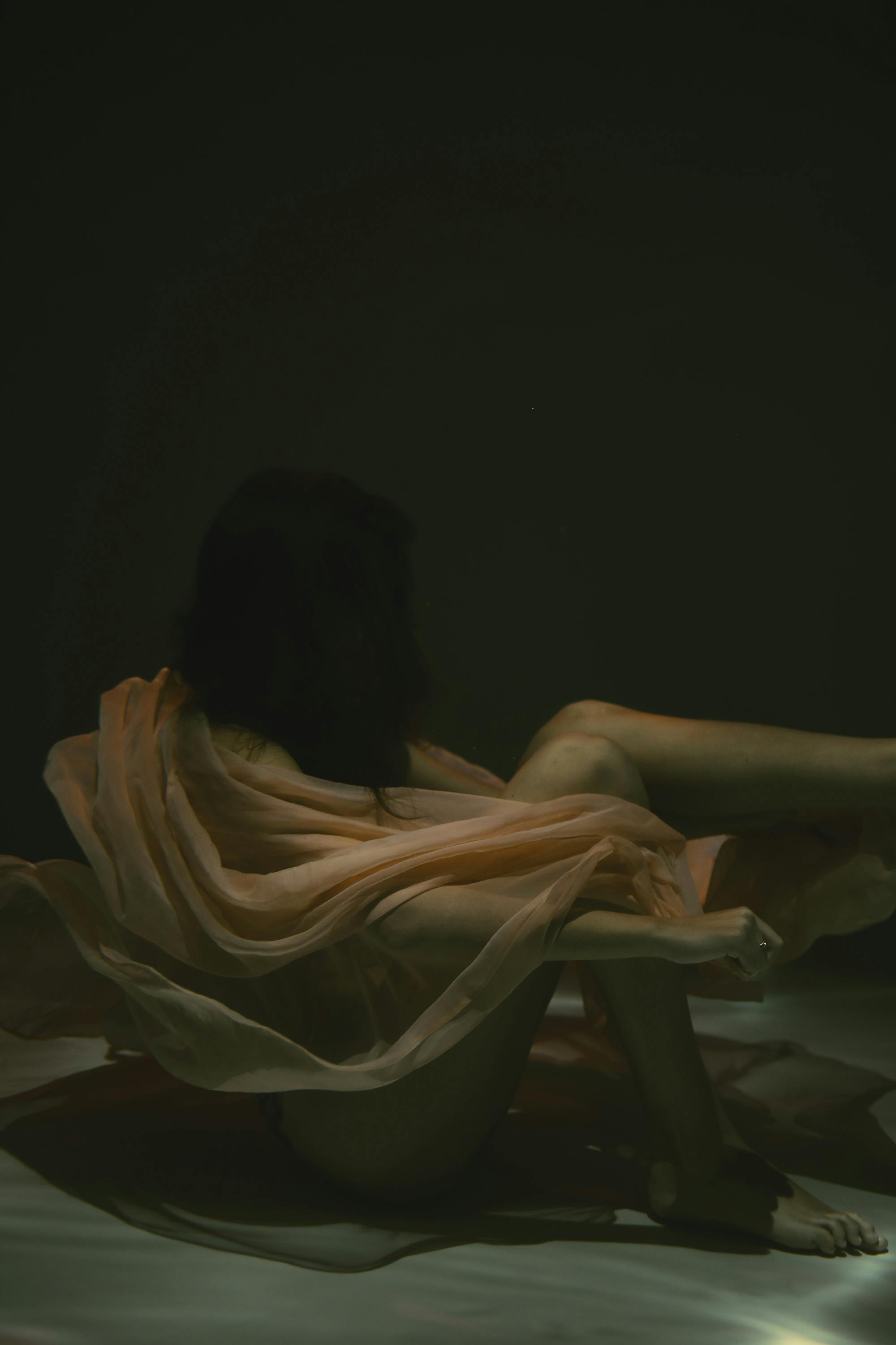 一个喜怒无常的女人，其水下肖像被流动的织物包裹，创造出一种超现实而空灵的效果