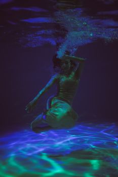 舞者沉浸在鲜艳的蓝绿灯光中，营造出梦幻般的氛围，这水下场景令人着迷