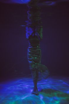一个人完全淹没在水下，迷人的黑暗和彩色光反射环绕着他