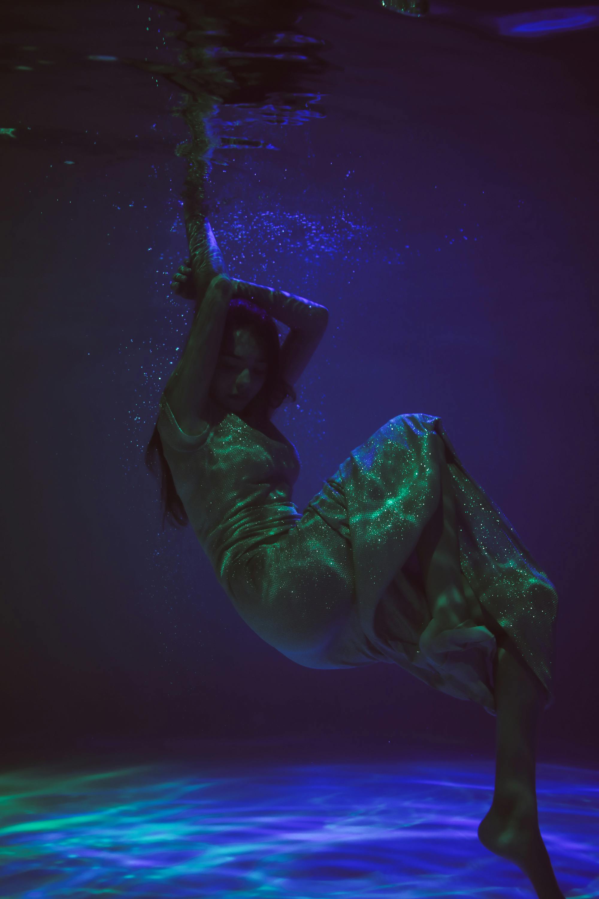 空灵的水下镜头中，一名身穿闪闪发光连衣裙的女子优雅漂浮