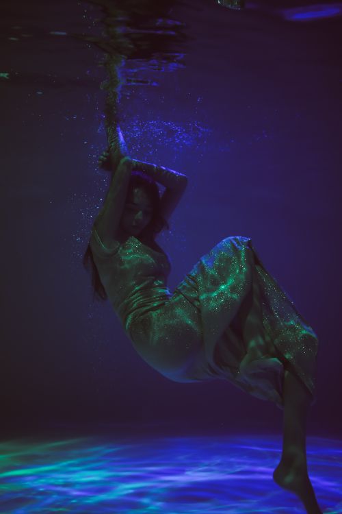 Free Ethereal underwater shot of a woman floating gracefully in a shimmering dress. Stock Photo