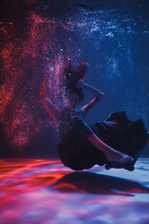 Free Artistic underwater shot of a woman posing gracefully in a swirl of vibrant red and blue colors. Stock Photo