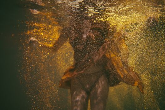 这是一张水下艺术镜头，一位被金色包裹的女性营造出超现实的氛围