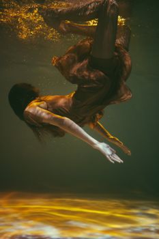 一位身着金色飘逸连衣裙的迷人女子，优雅地漂浮在水下