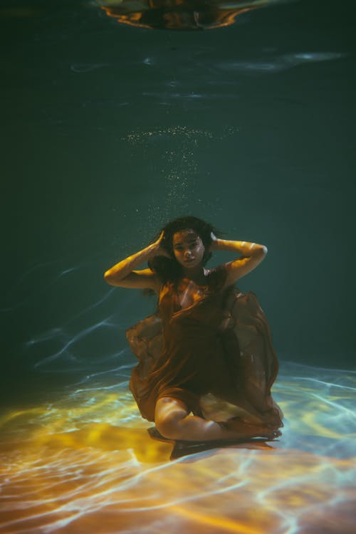 A Beautiful Woman Sitting Underwater Posing with Hands on Her Head