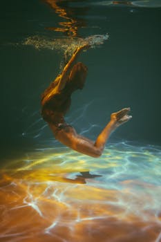 水下镜头中，一名女子优雅地游泳，阳光反射照亮了她