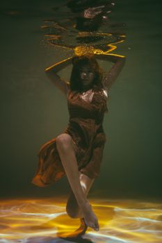 一位身着优雅流动衣裙的女子，在水下摆出迷人的肖像姿态，沐浴在金色的光芒中