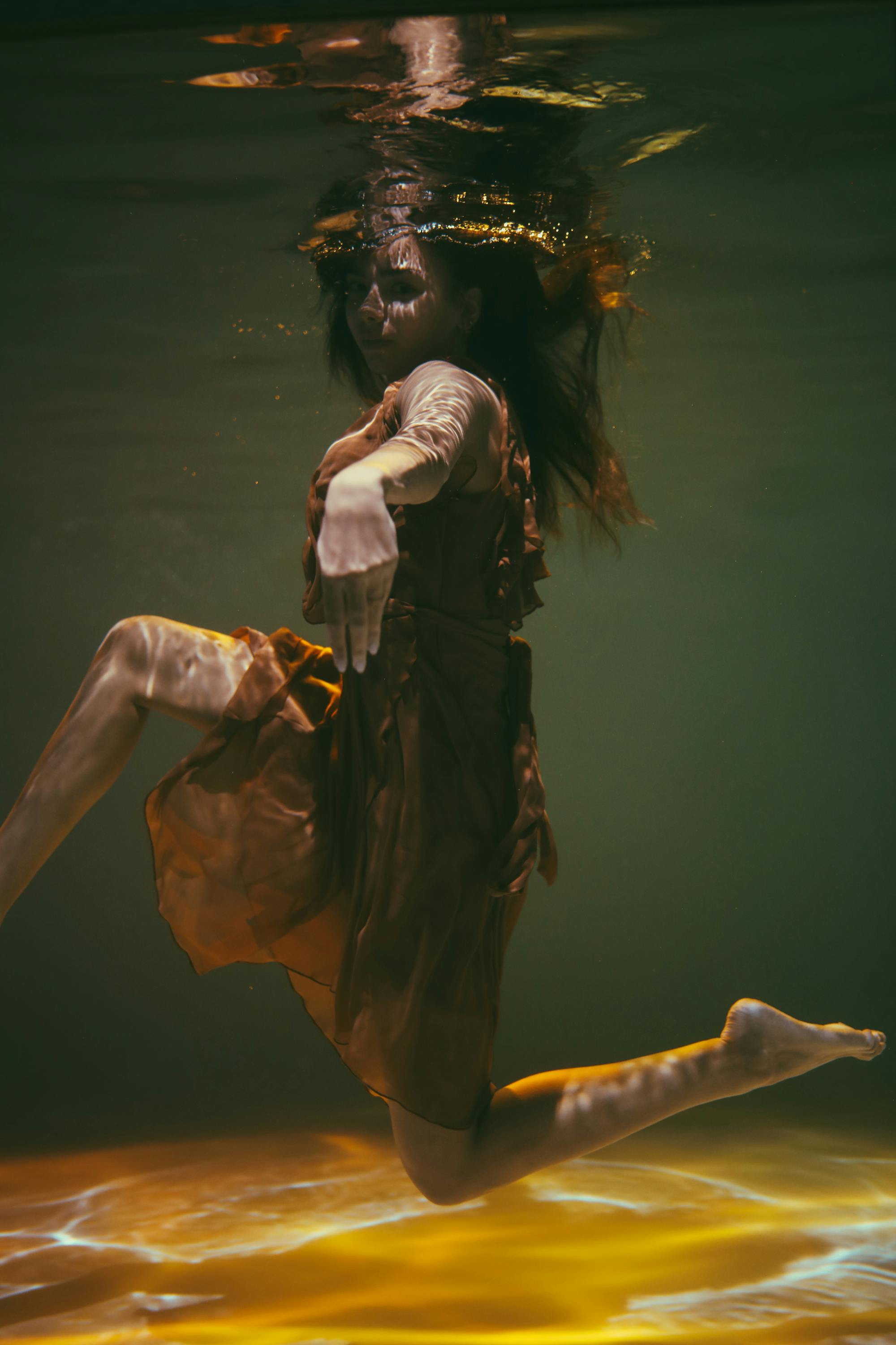 Artistic underwater photograph depicting a woman in a flowing dress striking a graceful pose.