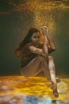 一位优雅的女子在漂浮的水下颗粒中摆出姿势，营造出宁静的美感