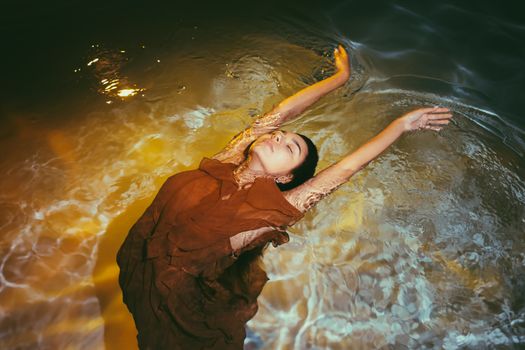 一位优雅的女子身着飘逸连衣裙，在温暖的夕阳下，平静地漂浮于水中