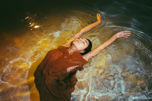 Free Elegant woman in flowing dress, floating peacefully in water under warm sunset light. Stock Photo