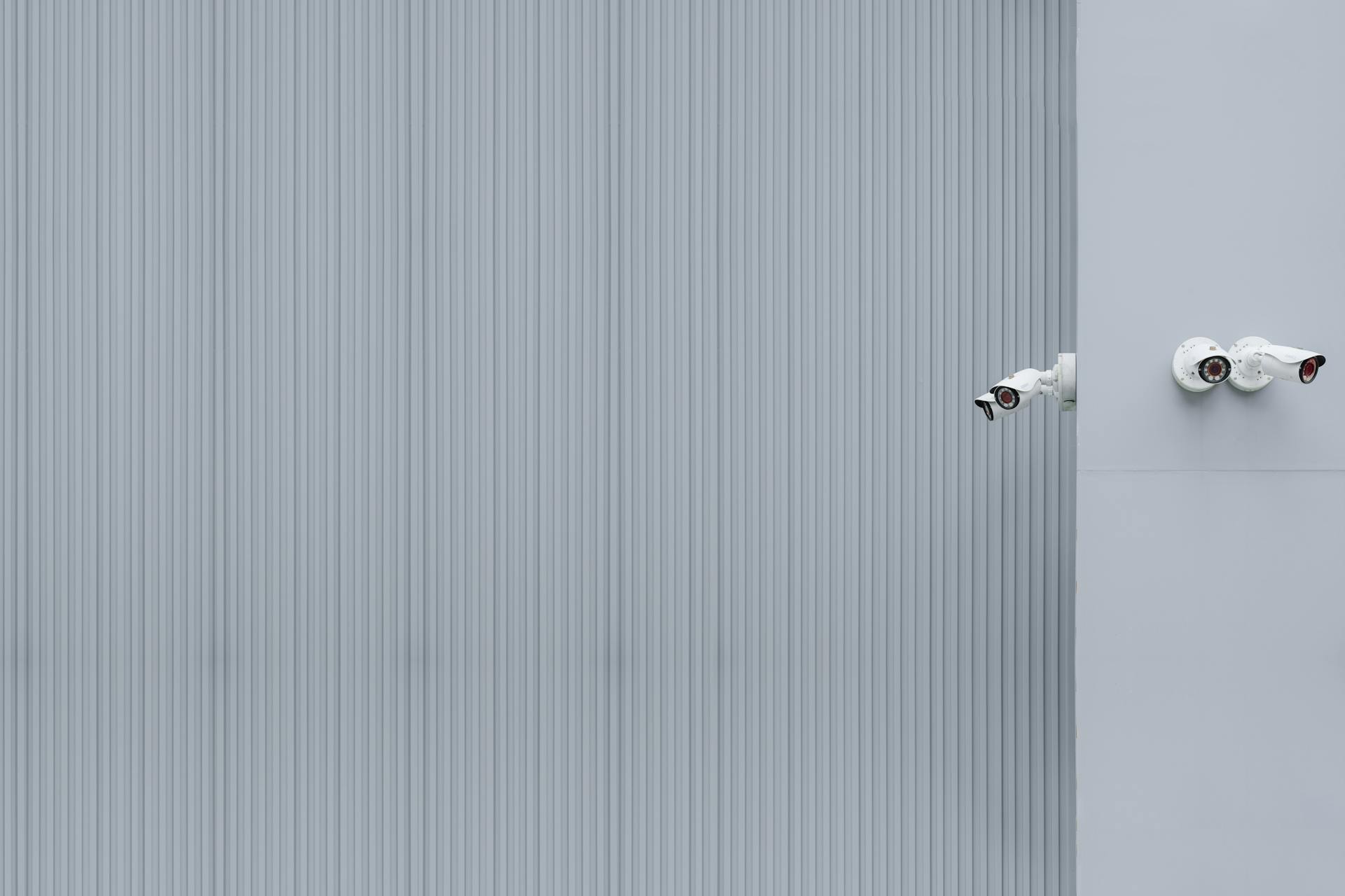 Two security cameras on a gray corrugated wall illustrating minimalism and surveillance.