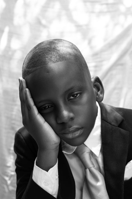 Black and white portrait of a young boy in a suit, deep in thought, resting his head on his hand.