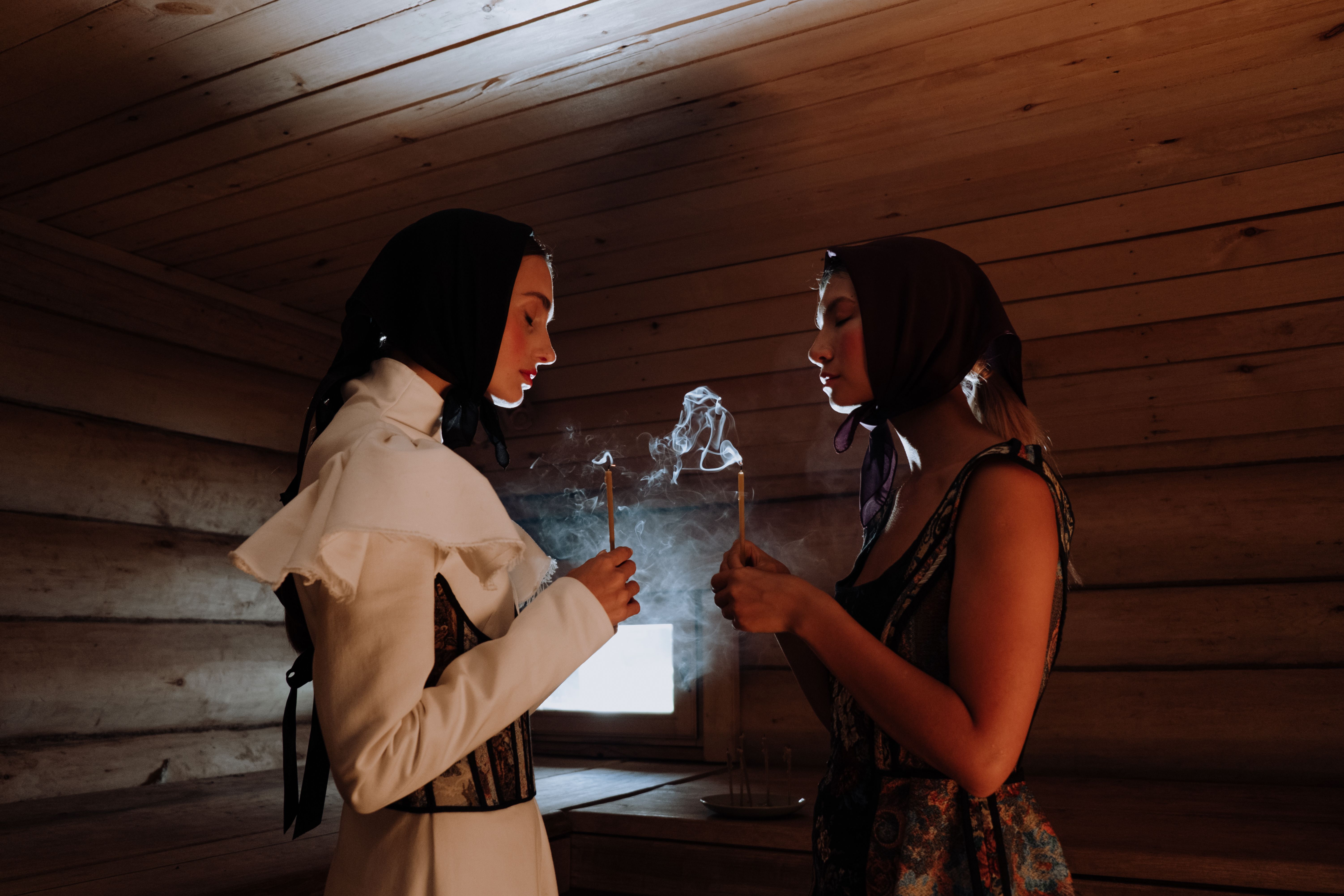 在一间木房内，两名女子手持香烛，四周烟雾缭绕，营造出一种神秘的氛围