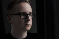 Close-up portrait of a man with eyeglasses in dim light, thoughtful expression.