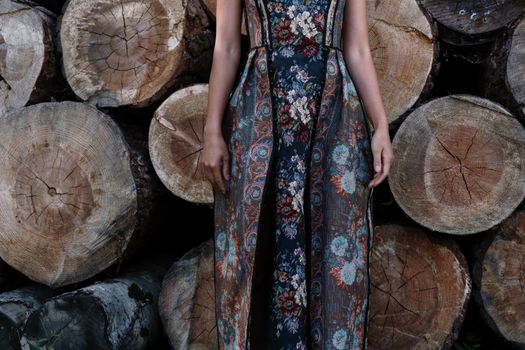 Close-up of a fashionable floral dress worn against stacked logs, combining nature and style.