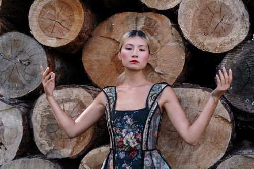 Free A stylish model in a floral dress poses gracefully in front of stacked wooden logs. Stock Photo