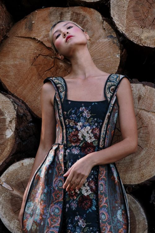 Free Stylish woman in a floral dress posing against a stack of wooden logs outdoors. Stock Photo