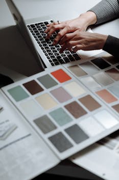 Hands typing on a laptop next to a color swatch book, ideal for design and creativity themes.