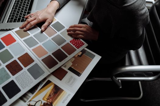 Interior designer on laptop reviewing color swatches for design project. Overhead view, modern workspace.