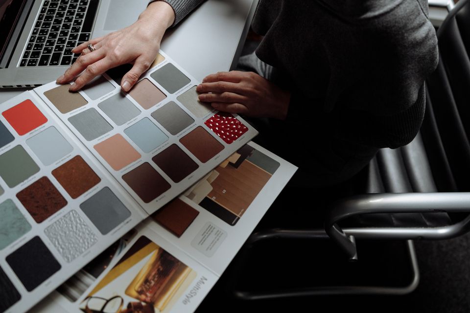Interior designer on laptop reviewing color swatches for design project. Overhead view, modern workspace.