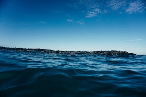 Blue rippling sea splashing near coastal city with residential buildings under blue cloudless sky