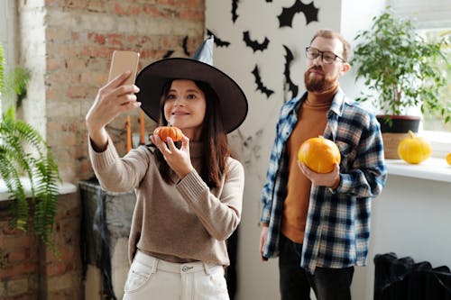 A Couple Holding Pumpkins While Taking Selfie Photo
