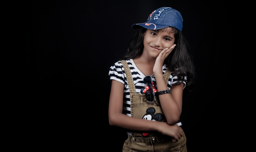 Free Cute Indian girl in casual attire posing confidently with a cap, smiling warmly in a studio setting. Stock Photo