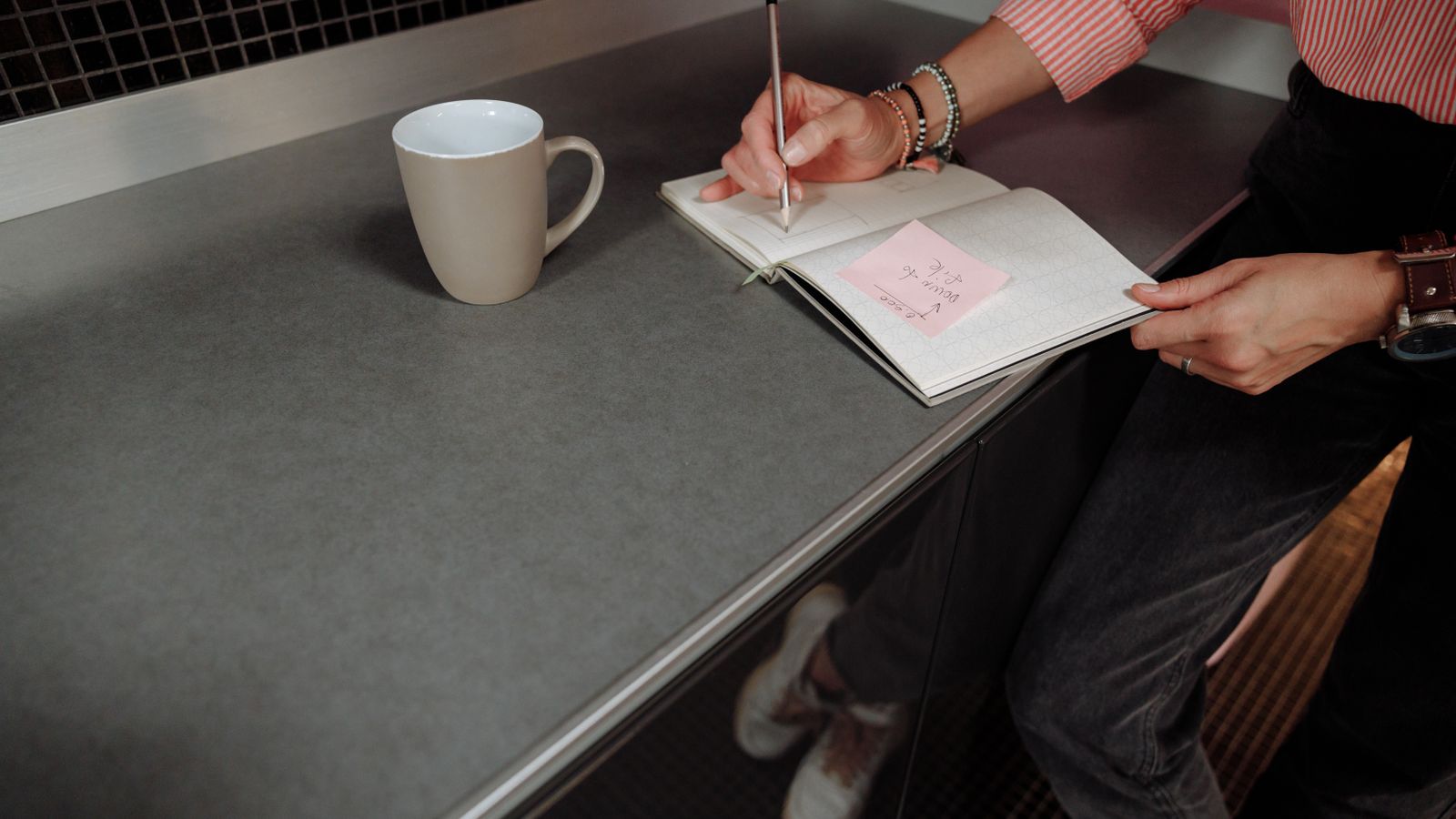 A person writing notes in an open notebook beside a coffee mug