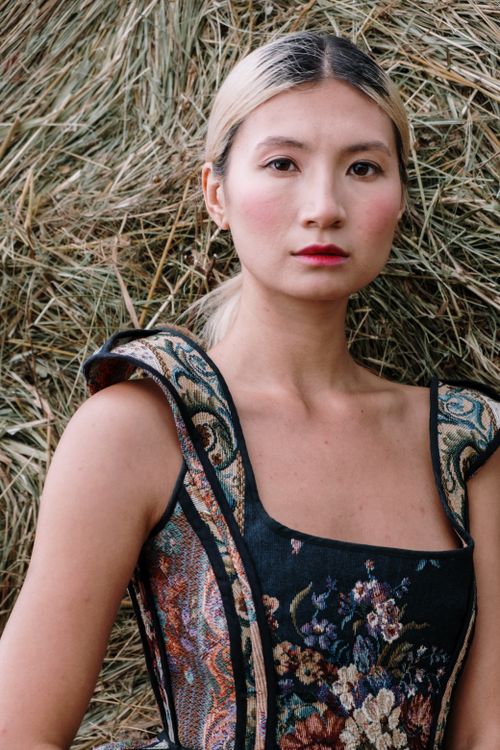 Free Artistic portrait of an elegant woman wearing a fashionable embroidered dress against a rustic hay background. Stock Photo