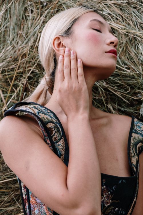 Free A serene portrait of a woman with eyes closed, posing elegantly outdoors in an ornate dress. Stock Photo