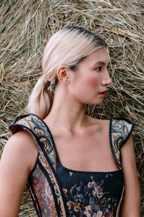 Free A side profile portrait of a blonde woman in a floral dress posing against hay. Stock Photo