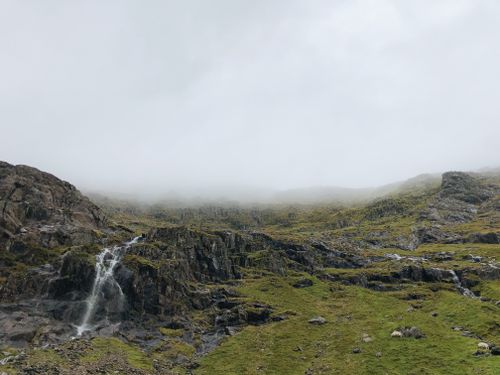 Free A scenic view of a waterfall flowing through the rocky mountains under a cloudy sky in Gwynedd, Wales. Stock Photo