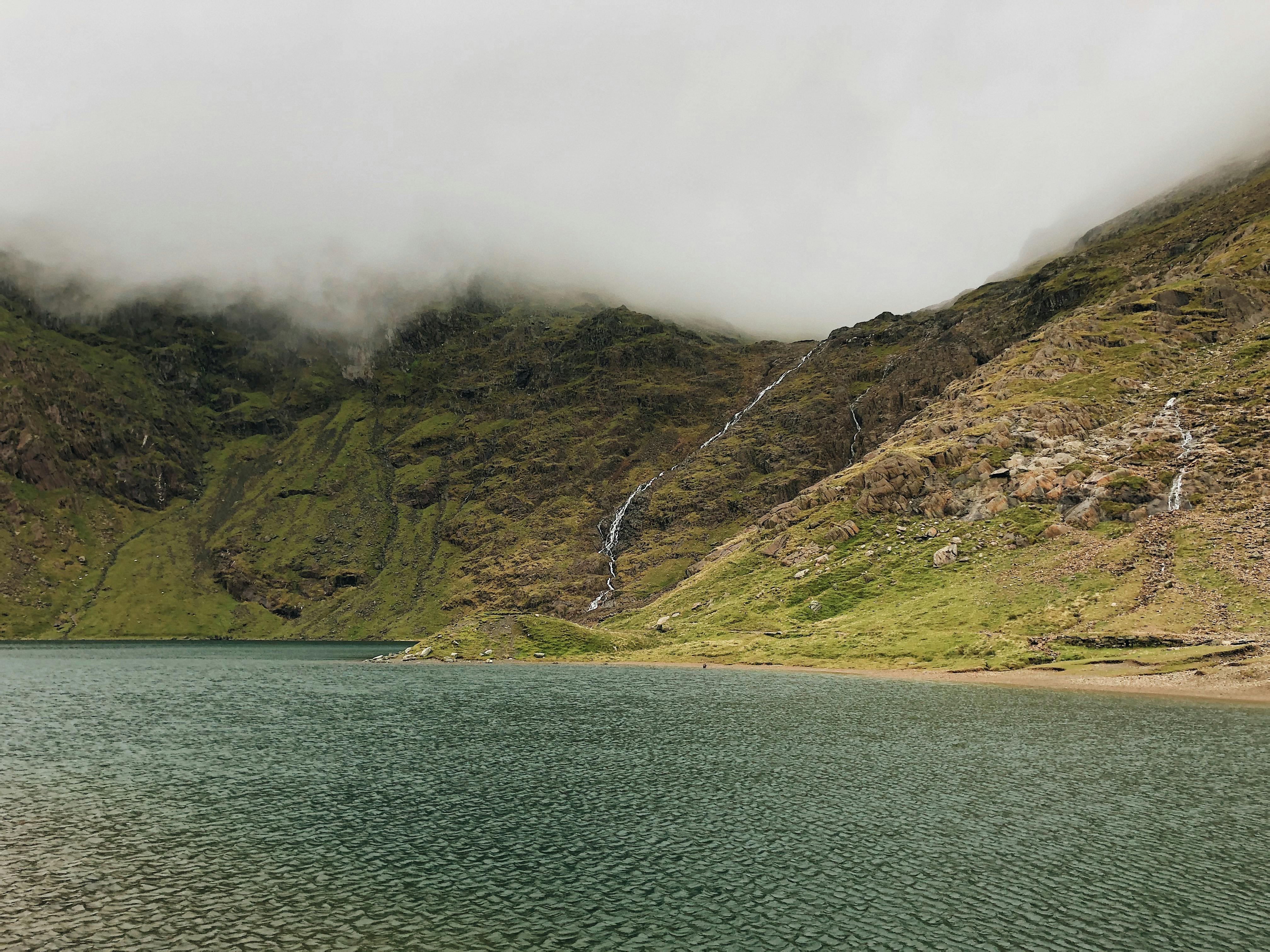 Tranquil mountain lake view in Gwynedd, showcasing lush green hills and misty skies.