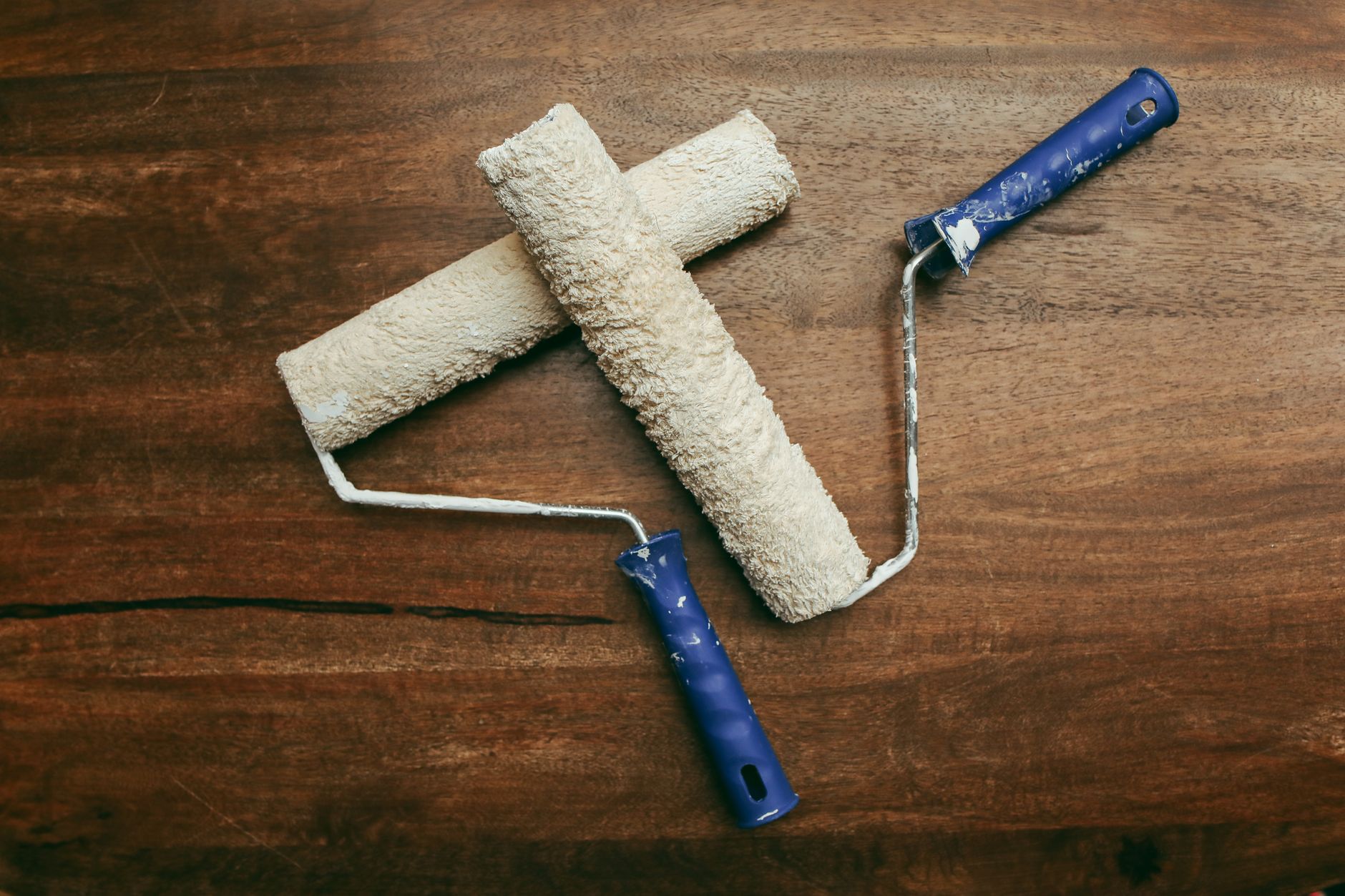Two used paint rollers with blue handles on a wooden surface, seen from above.