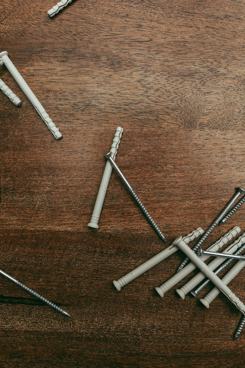 Fastener Selection for DIY Woodworking – Screws and Anchors Organized on a Work Surface Flat lay of various screws and plastic anchors scattered on a wooden surface for DIY fastener selection