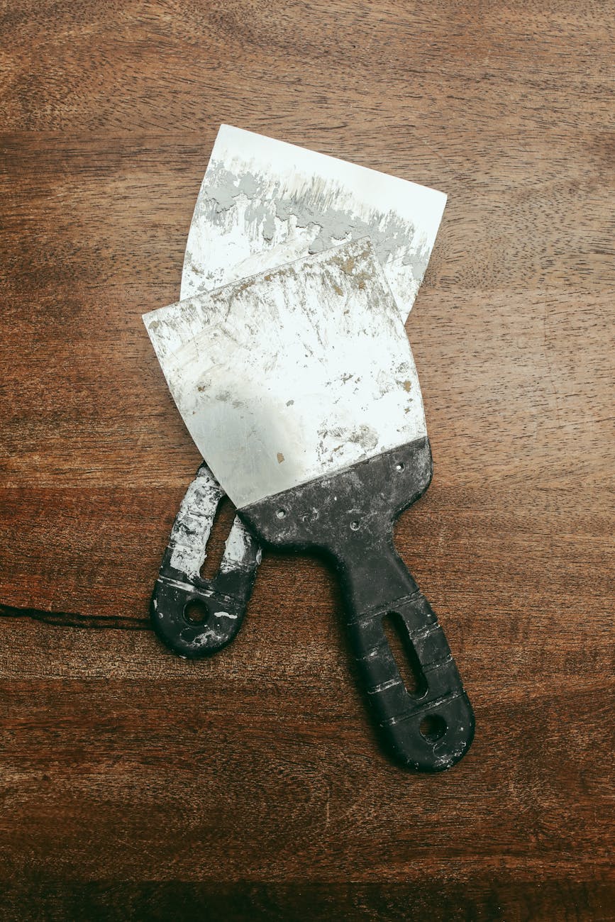 Close-up of two worn metal spatulas lying on a textured wooden surface.