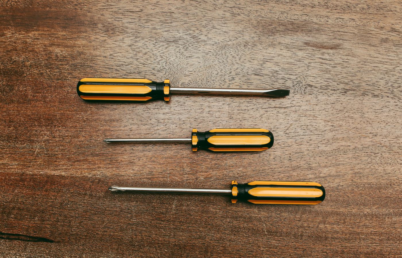Flat lay of three screwdrivers on a wooden table, showcasing different types.