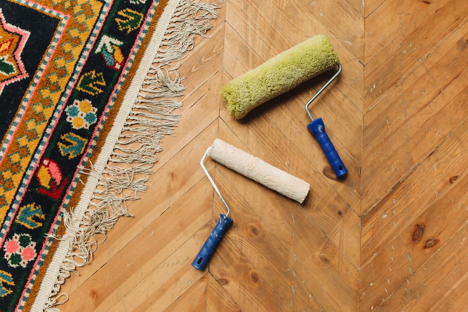 Two paint rollers on a wooden floor next to a colorful rug, symbolizing home renovation.