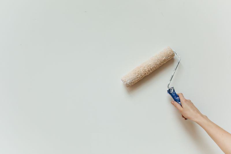 Mão aplicando tinta com rolo na parede