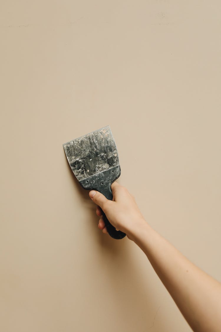 Hand Holding Renovation Tool Near Wall