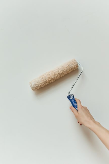 A hand applying paint on a wall using a roller brush; minimalistic home renovation scene.