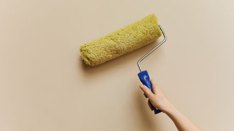A hand using a yellow paint roller to paint a beige wall. Perfect for DIY and home improvement themes.