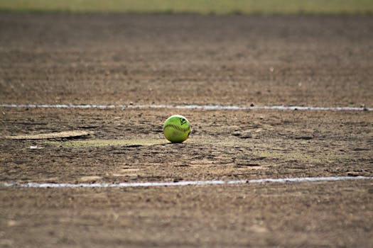 A lone softball sits on a dusty field, capturing the essence of the sport.