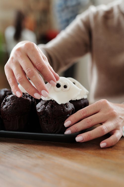 Person Holding Chocolate Cupcake With White Icing on Black Plate