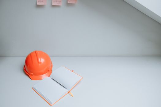 这个极简主义的工作空间非常适合概念设计，桌上放着一顶橙色安全帽和一台打开的笔记本电脑