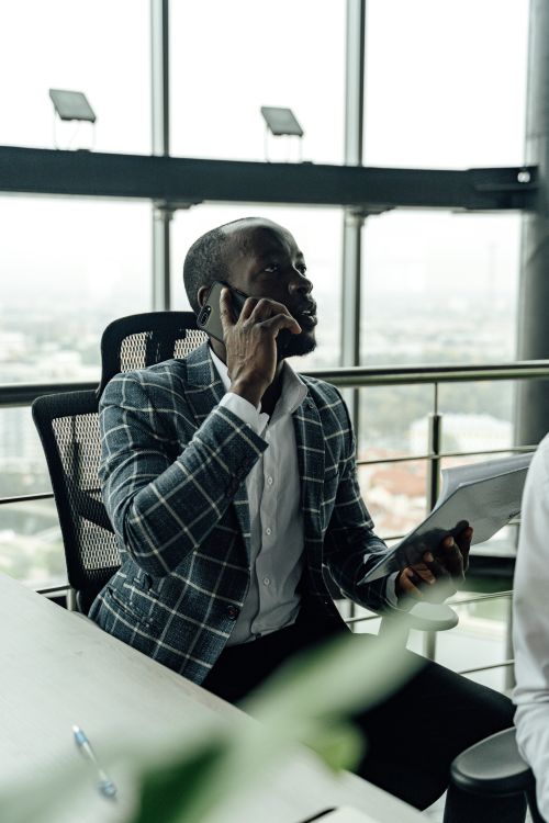 Free Focused businessman talking on smartphone while holding a document in a modern office setting. Stock Photo