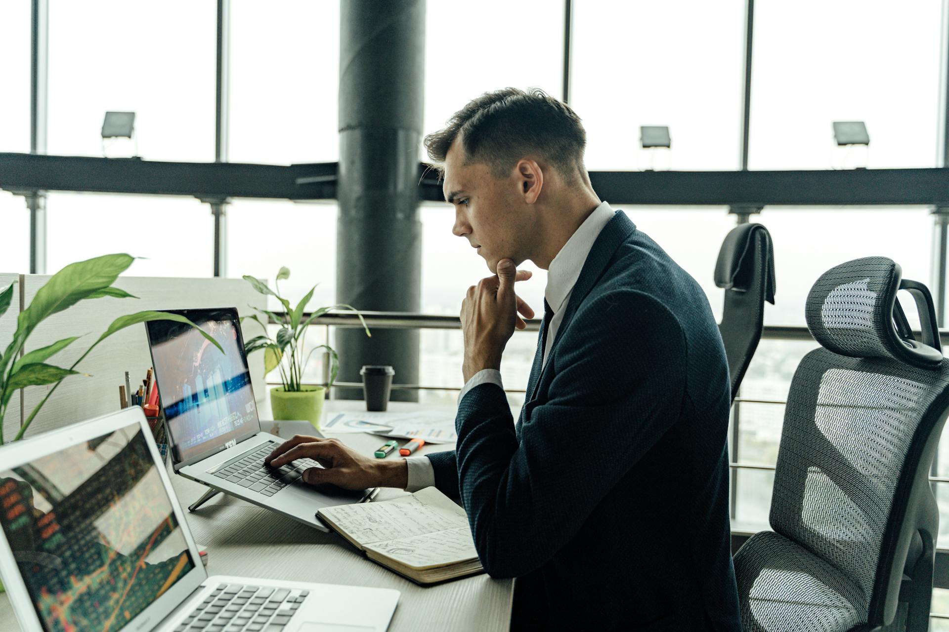 Professional man analyzing stock market data at modern office workspace with laptops.