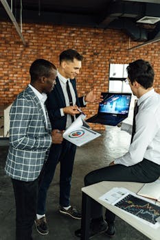 Three business professionals discussing financial charts in a modern office setting.