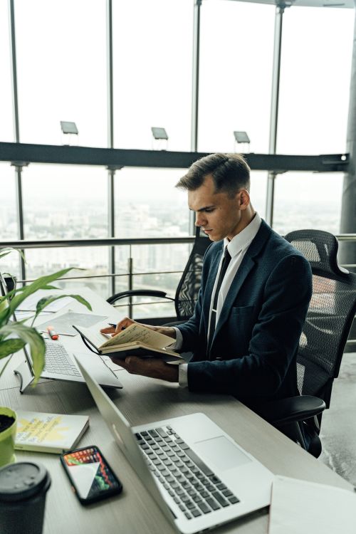 Free Businessman in black suit reading in a modern office with laptop. Stock Photo